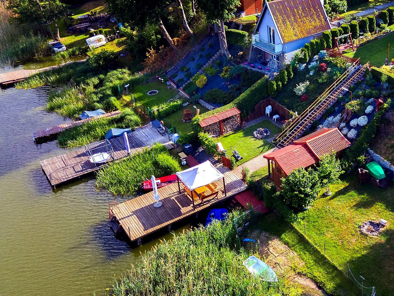 Widok z góry na pomost, łódki, ogród i zejście do jeziora